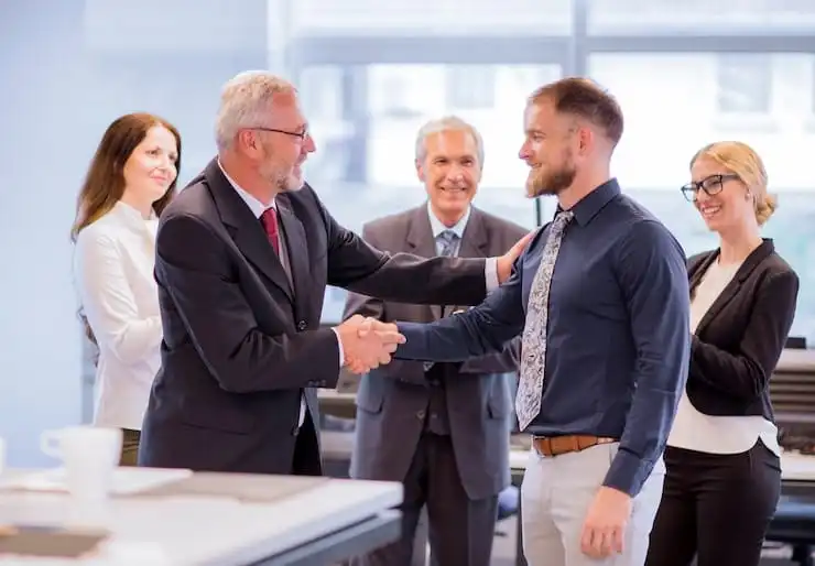 Business professionals congratulating a new employee with a handshake during a corporate meeting.